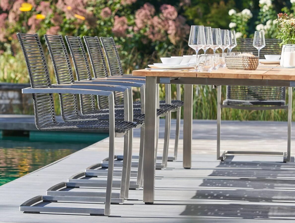 Ein eleganter, gedeckter Teakholztisch mit Edelstahlgestell und Freischwinger-Gartensesseln auf einer Terrasse