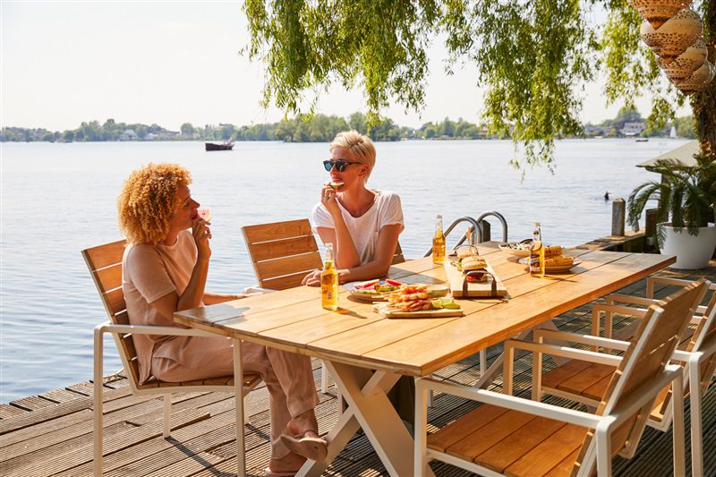 Zwei Frauen auf Teakholzstühlen an Gartentisch am Wasser sitzend