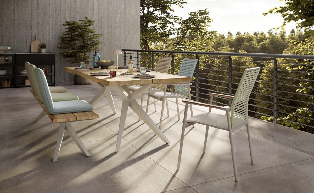 Tischgruppe mit Sitzbank und Stühlen in Pastellfarben und mit Holz-Elementen auf einer modernen Terrasse